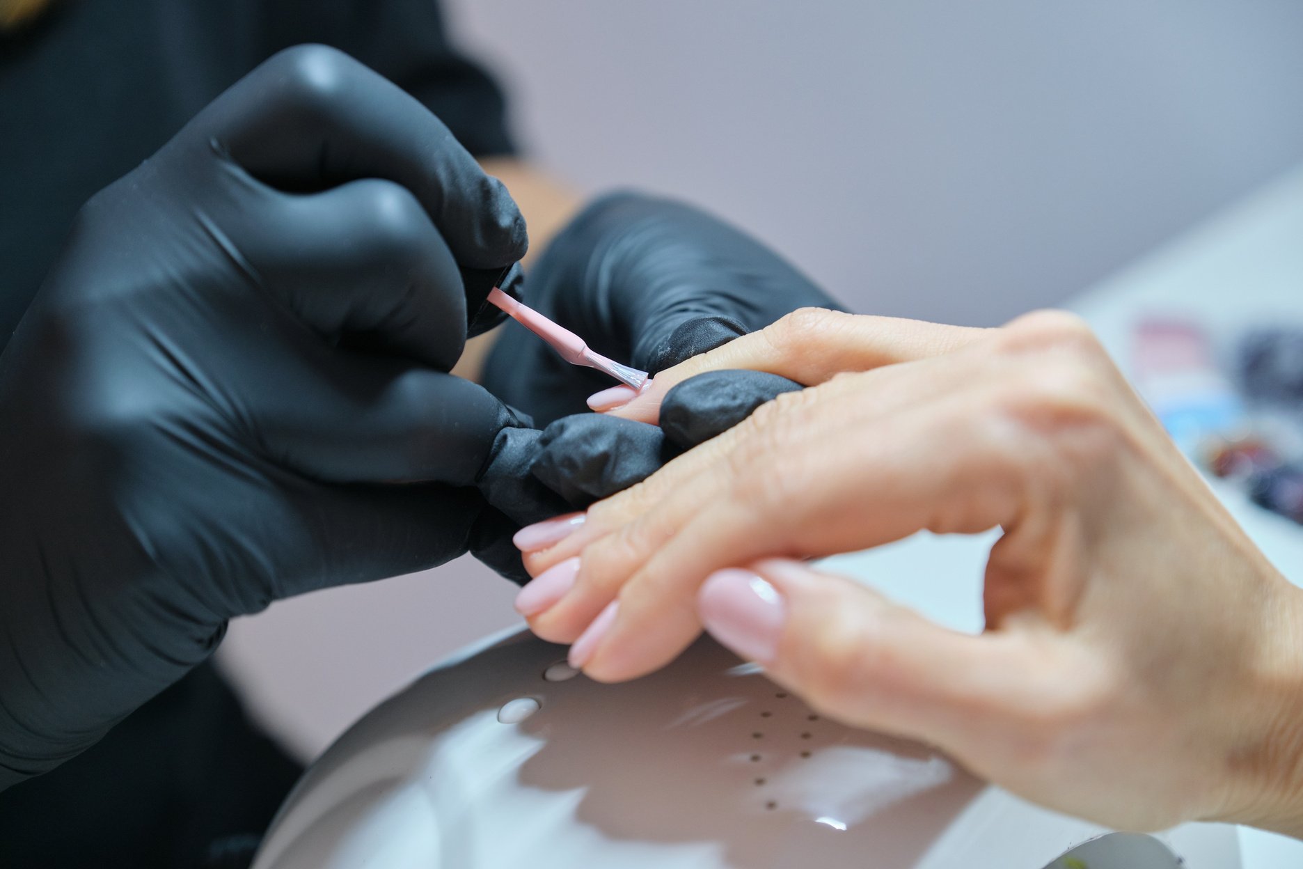 Manicurist varnishes gel nails. Professional hand and nail care in beauty salon